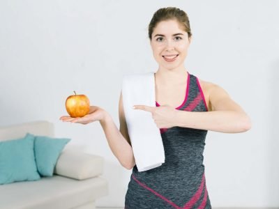 smiling-portrait-fitness-young-woman-pointing-her-finger-toward-whole-fresh-apple-min